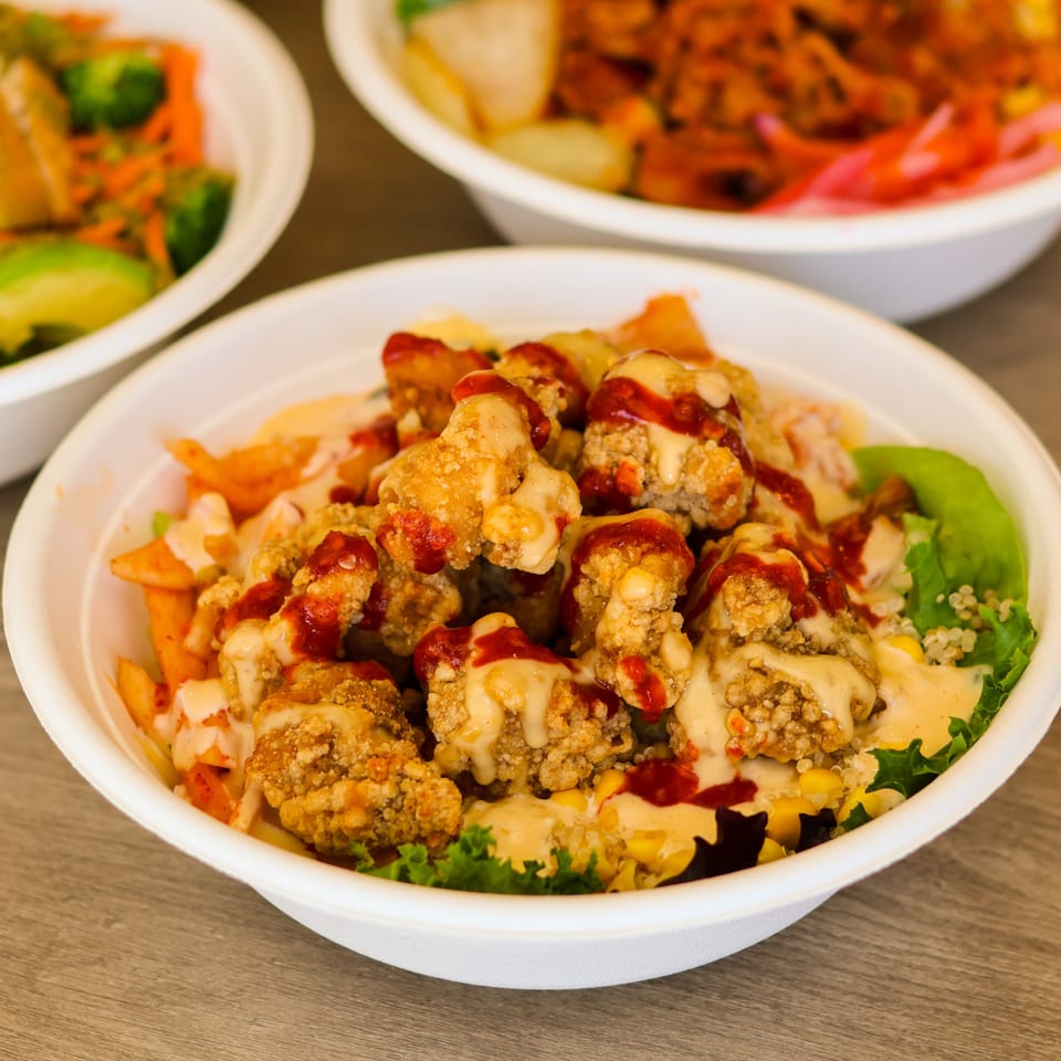 Crispy fried bites with two sauces, corn, quinoa, and lettuce in a white bowl.