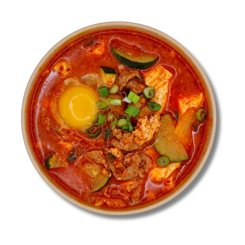 Spicy red Korean stew with egg yolk, beef, tofu, zucchini, and green onions.